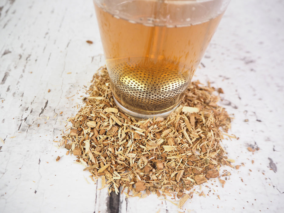 Frisch aufgebrühter Eichenrindentee in einer Tasse mit Teesieb, umgeben von losen Kräutern, traditionelle Wellness-Teezubereitung.